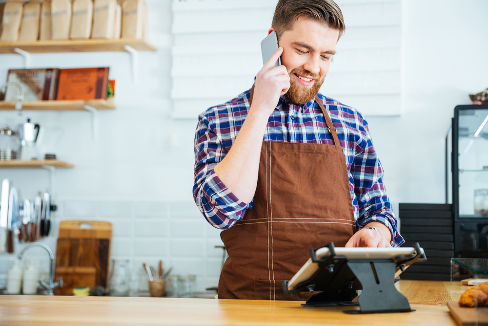 https://5565770.fs1.hubspotusercontent-na1.net/hubfs/5565770/Handsome%20smiling%20barista%20with%20beard%20taking%20order%20on%20cell%20phone%20and%20using%20tablet%20in%20cafeteria.jpeg
